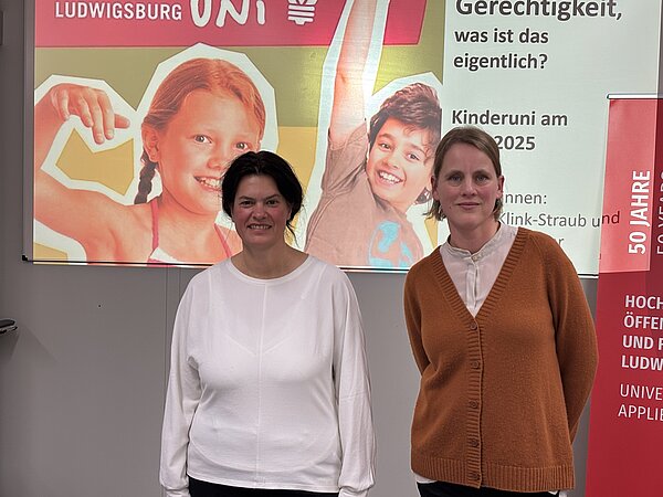 Prof. Dr. Judith Klink-Straub und Anne Kraushaar, die Dozentinnen der Kinderuni 2025, lächeln vor der HVF-Projektionswand.