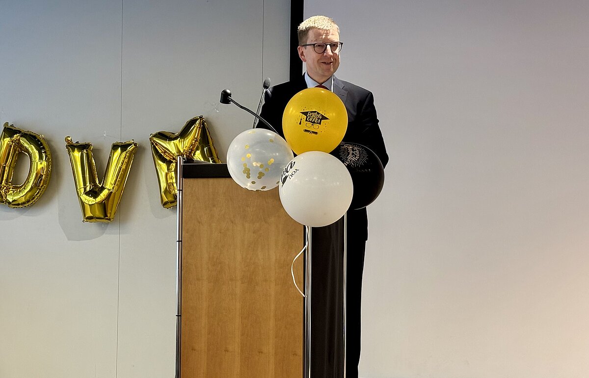 Dr. Daniel O’Sullivan begrüßt die Gäste von einem Rednerpult aus, mit "DVM"-Ballons und Dekor im Hintergrund.