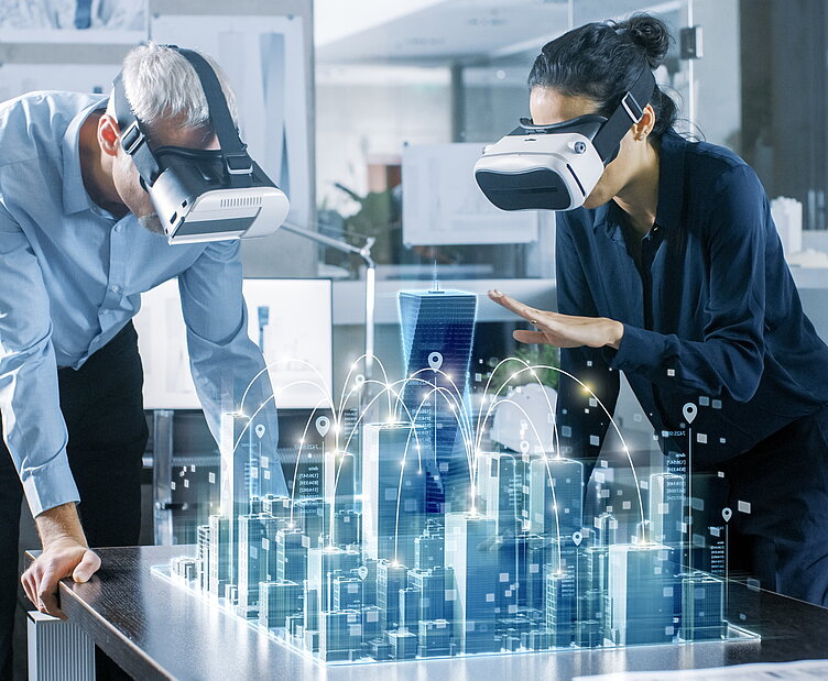 Zwei Personen mit VR-Headsets betrachten ein holografisches 3D-Stadtmodell auf einem Tisch, das eine vernetzte Smart City darstellt.