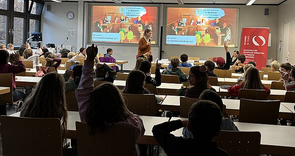 Anne Kraushaar, Journalistin, spricht bei der Kinderuni HVF mit vielen Kindern im Hörsaal, die strecken.