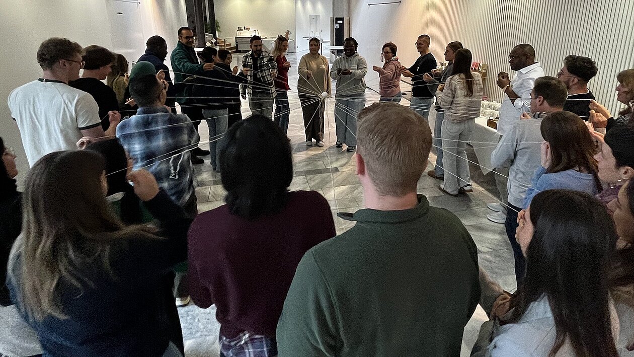 KIKS-Projekt "Perspektivwechsel 2025": Studierende und Zugewanderte stehen im Kreis, halten Fäden in den Händen