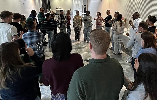 KIKS-Projekt "Perspektivwechsel 2025": Studierende und Zugewanderte stehen im Kreis, halten Fäden in den Händen