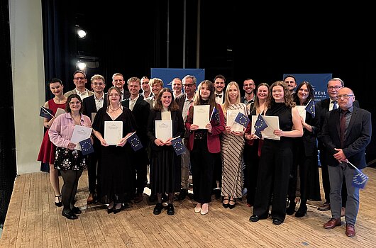 Stolze Absolventen des Master Europäischen Verwaltungsmanagement (MEPA) posieren mit Urkunden und EU-Flaggen.