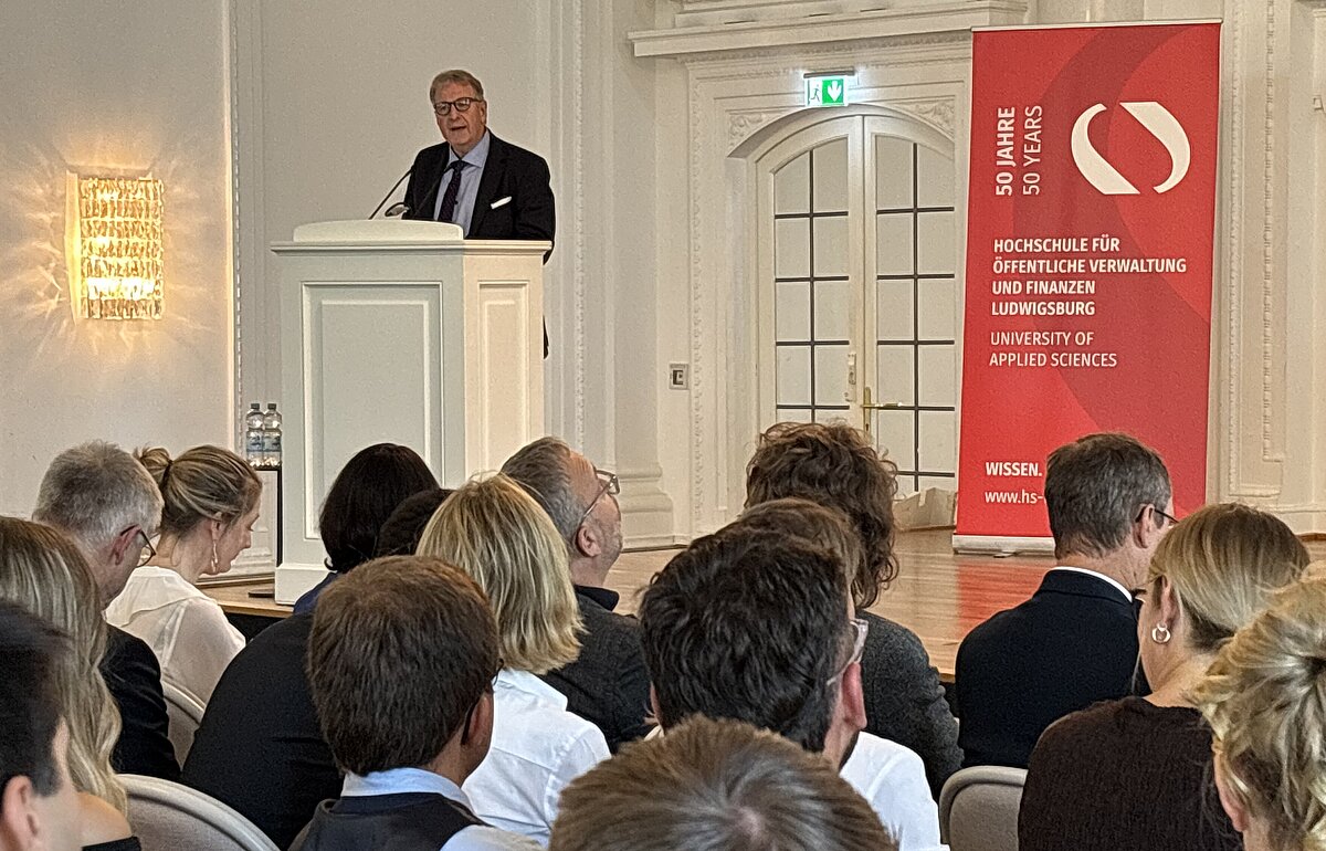 Professor Elmar Vogl hält als Vertreter der Ralf-Wuttke-Stiftung eine Rede vor einem großen Publikum bei der Bachelorfeier.
