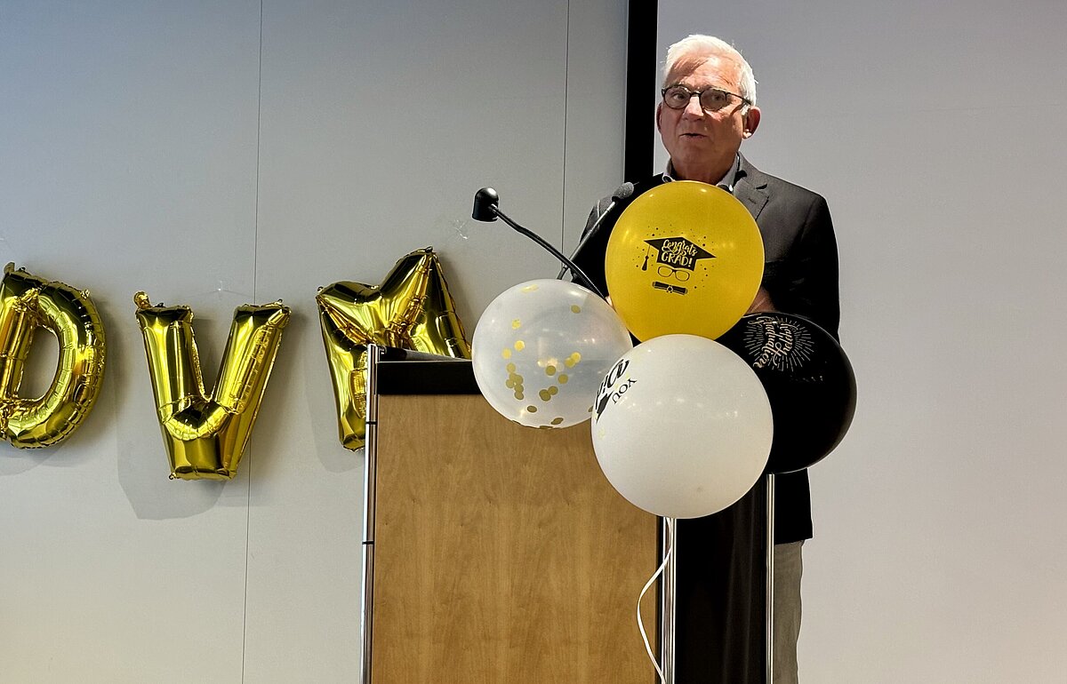 Thomas Strobl spricht an einem Pult mit Ballons und "DVM"-Buchstabenballons im Hintergrund.