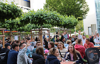 Hochschulangehörige auf Biertischgarnituren im Innenhof der HVF