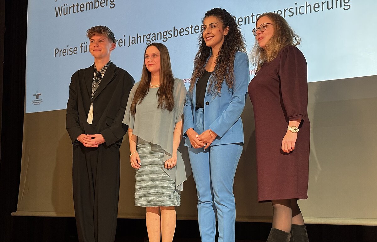 Ministerialdirektorin Leonie Dirks (r.) ehrt die drei Jahrgangsbesten (Georgia Toulkeridis, Julia Kerti und Jan Neubauer) auf der Bühne.