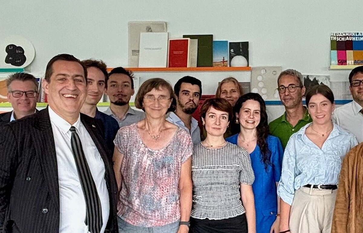 Gruppenfoto von 17 Teilnehmenden im Generalkonsulat vor Bücherregalen und einem Roll-up des Institut français.