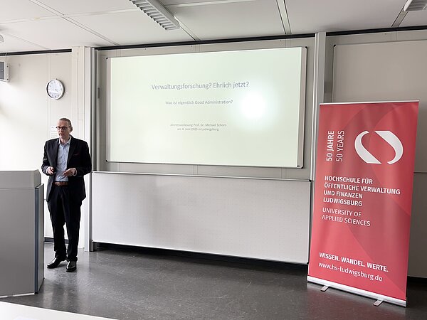 Antrittsvorlesung Prof. Dr. Michael Schorn an der HVF Ludwigsburg Professor Schorn hält seine Antrittsvorlesung über Verwaltungsforschung vor einem Whiteboard mit Präsentation und HVF-Banner.