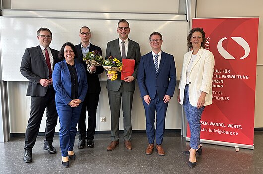 Akademische Feier der HVF Ludwigsburg mit Honorarprofessoren Das Rektorat und die neu ernannten Honorarprofessoren posieren lächelnd vor einer weißen Wand und einem HVF-Banner.