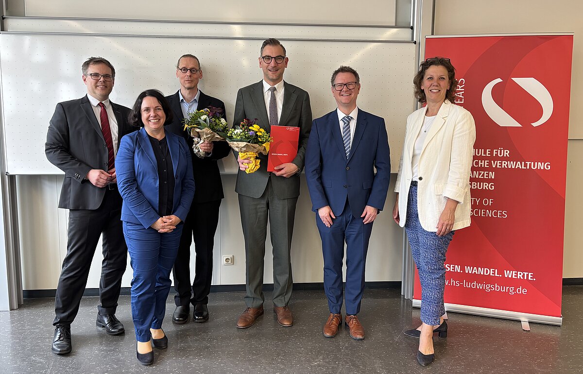 Akademische Feier der HVF Ludwigsburg mit Honorarprofessoren Das Rektorat und die neu ernannten Honorarprofessoren posieren lächelnd vor einer weißen Wand und einem HVF-Banner.