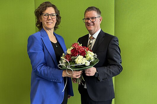 Rektorin HVF Rauskala und Kanzler Dammler mit Blumenstrauß vor grüner Wand.