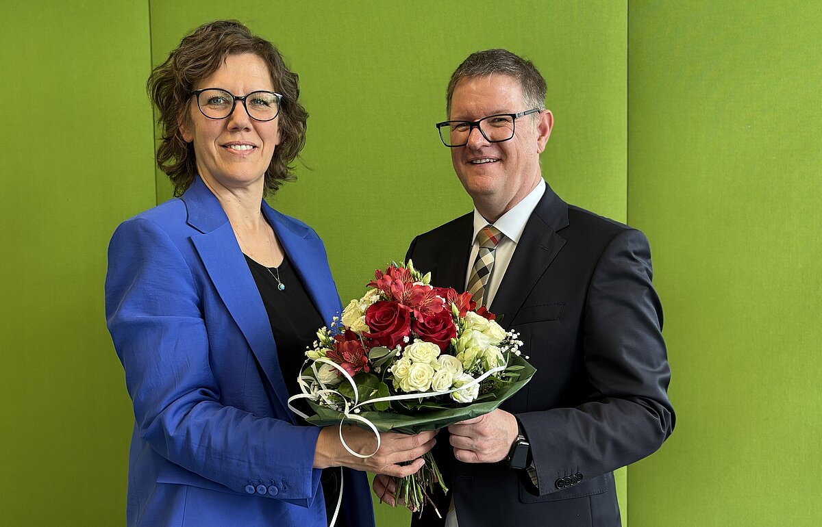 Rektorin HVF Rauskala und Kanzler Dammler mit Blumenstrauß vor grüner Wand.