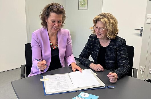 Petra Hasebrink, Landesdirektorin Baden-Württemberg der BBBank (links), und Rektorin Dr. Iris Rauskala (rechts) sitzen an einem Tisch und unterzeichnen den Sponsoringvertrag.