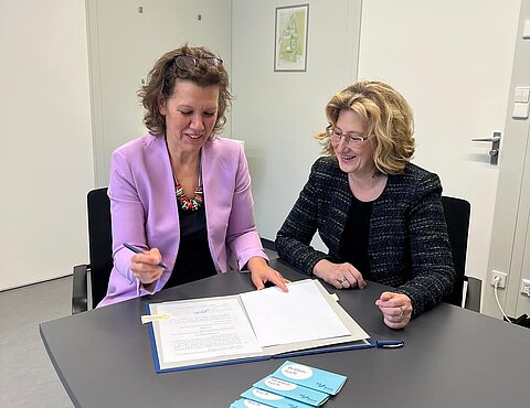 Petra Hasebrink, Landesdirektorin Baden-Württemberg der BBBank (links), und Rektorin Dr. Iris Rauskala (rechts) sitzen an einem Tisch und unterzeichnen den Sponsoringvertrag.