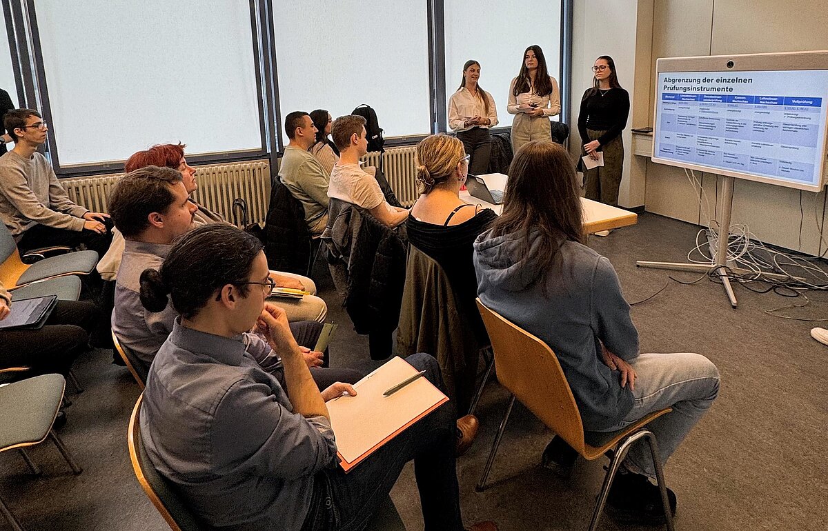 Zwei Studierende der HVF Ludwigsburg stellen den im Rahmen eines Wahlpflichtfachs entwickelten Einarbeitungsleitfaden vor erfahrenen Praktiker:innen des Finanzamts vor.