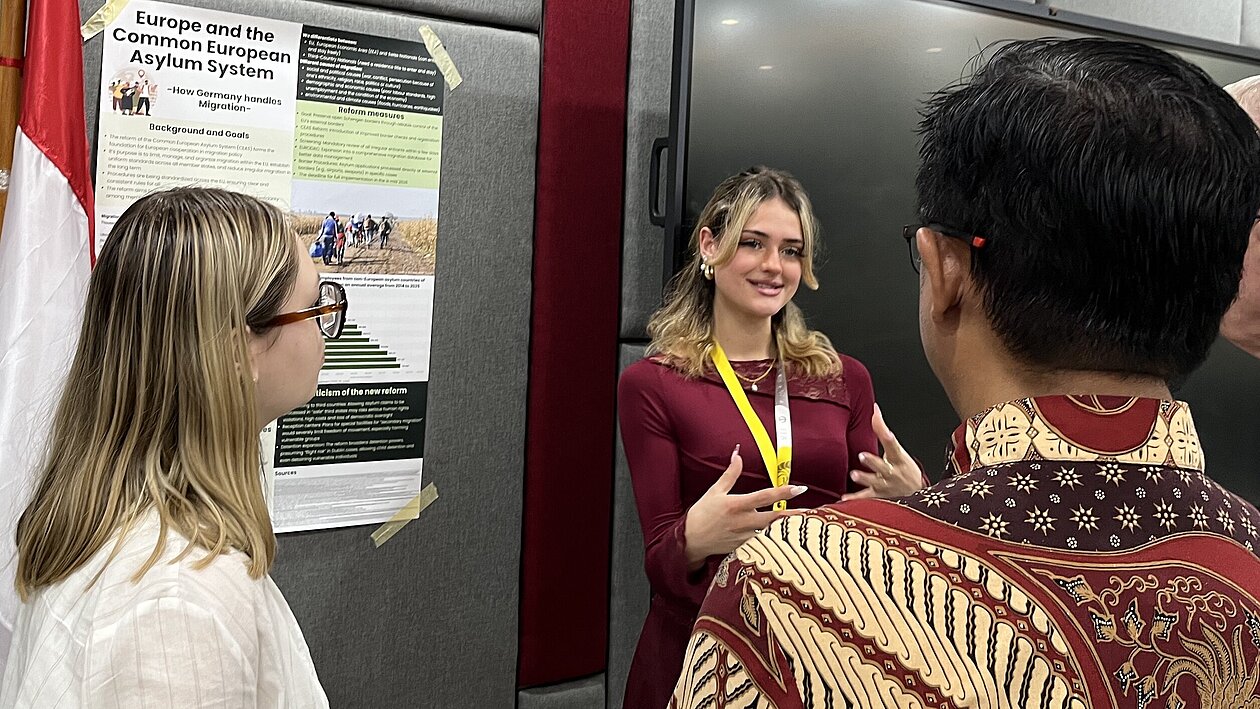 Studentin präsentiert ein wissenschaftliches Poster zum europäischen Asylsystem vor indonesischen Forschenden beim BRIN.