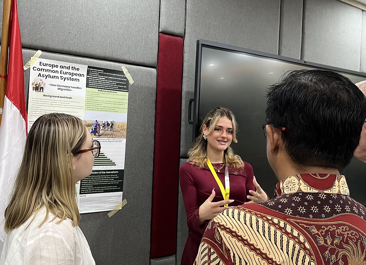 Studentin präsentiert ein wissenschaftliches Poster zum europäischen Asylsystem vor indonesischen Forschenden beim BRIN.