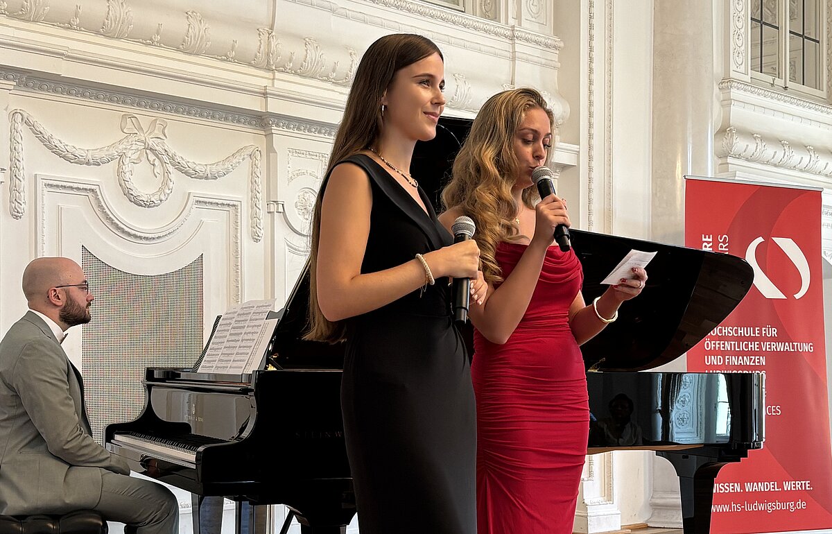Die Moderatorinnen Cayenne Striegel (links, schwarzes Kleid) und Morena Cioffi (rechts, rotes Kleid) mit Musiker Lukas Buhl (links, am Flügel) bei der Eröffnung.
