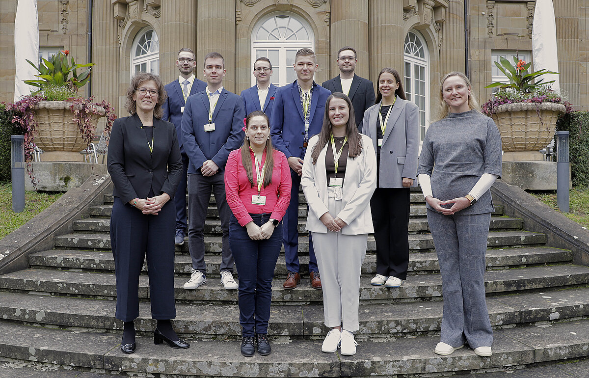 Gruppenfoto von zehn Absolvent:innen, Rektorin Dr. Iris Rauskala (l.) und Leiterin Ulrike Hess (r.) auf einer Steintreppe vor der Villa Reitzenstein.