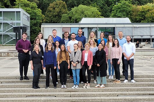 Neue Master-Studierende des Studiengangs Public Management stehen für ein Foto auf einer Treppe am Campus