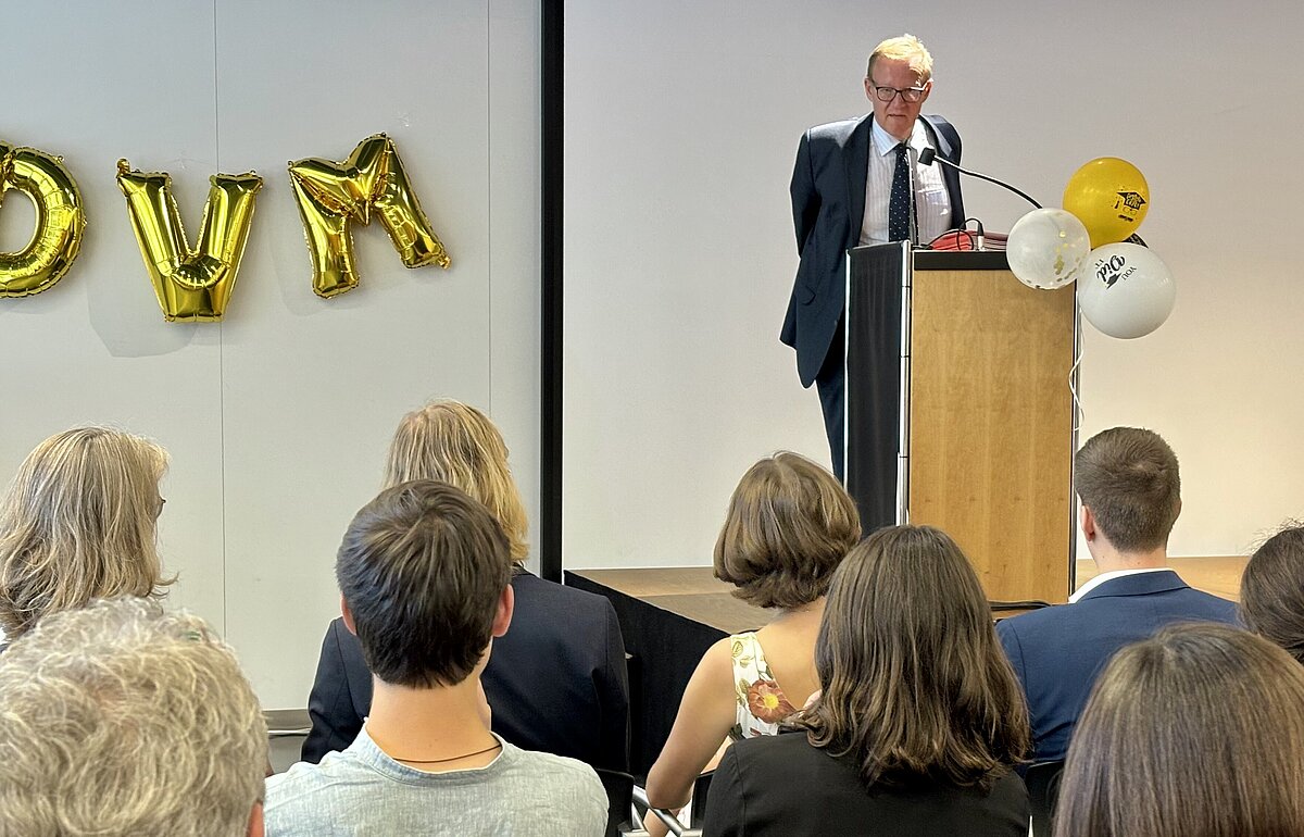 Studiendekan Prof. Dr. Müller-Török spricht vom Pult aus. Im Vordergrund sind die Hinterköpfe der Zuhörer zu sehen.