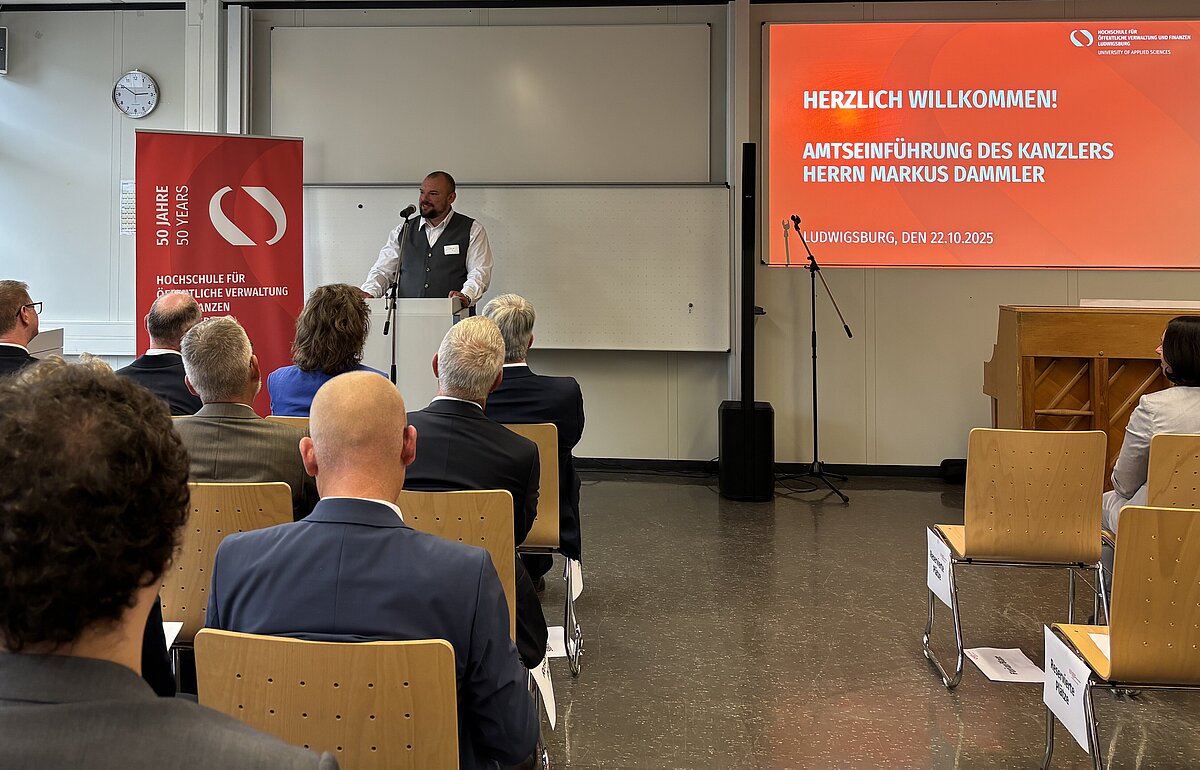 Florian Blatt, Vorsitzender des Personalrats der HVF, hält ein Grußwort zur Amtseinführung von Kanzler Markus Dammler vor dem Publikum.