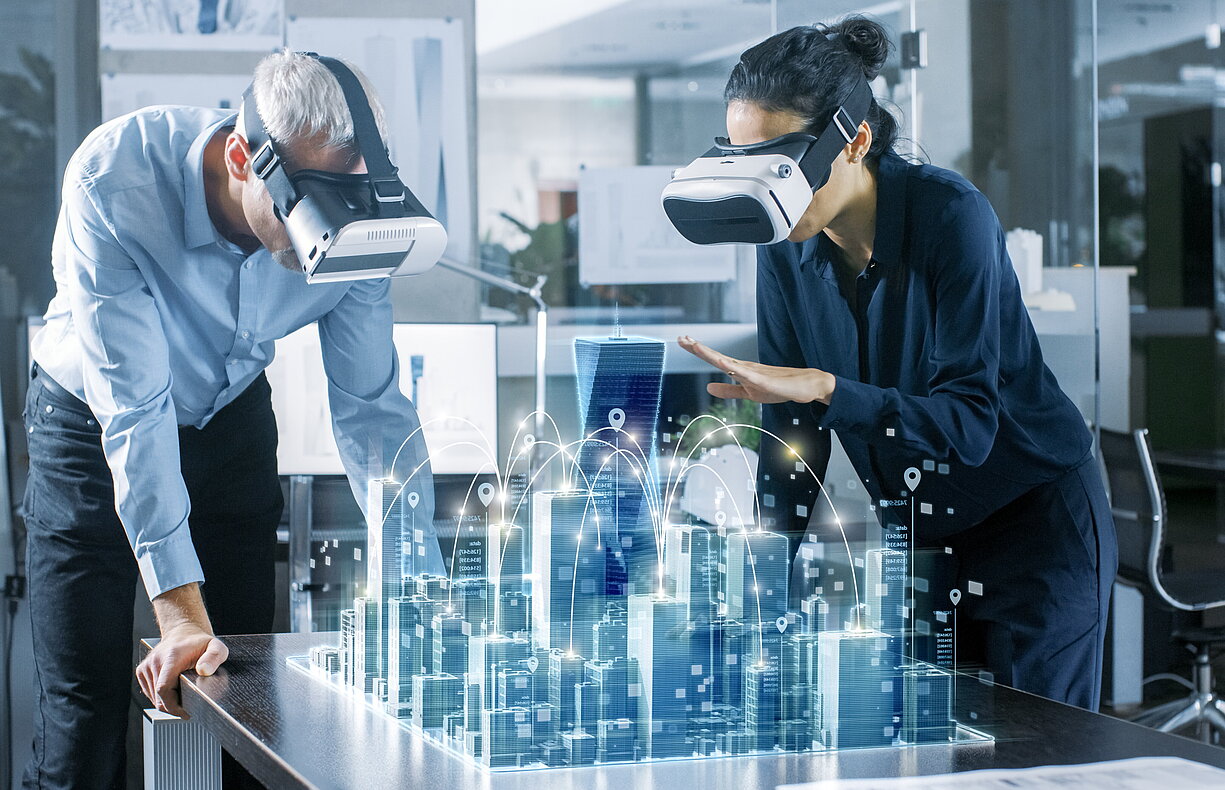 Zwei Personen mit VR-Headsets betrachten ein holografisches 3D-Stadtmodell auf einem Tisch, das eine vernetzte Smart City darstellt.