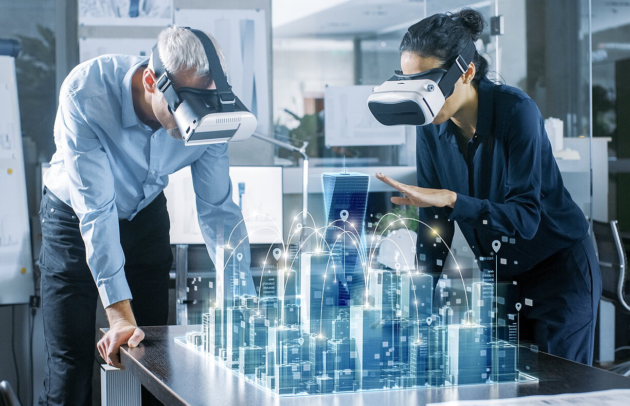 Zwei Personen mit VR-Headsets betrachten ein holografisches 3D-Stadtmodell auf einem Tisch, das eine vernetzte Smart City darstellt.
