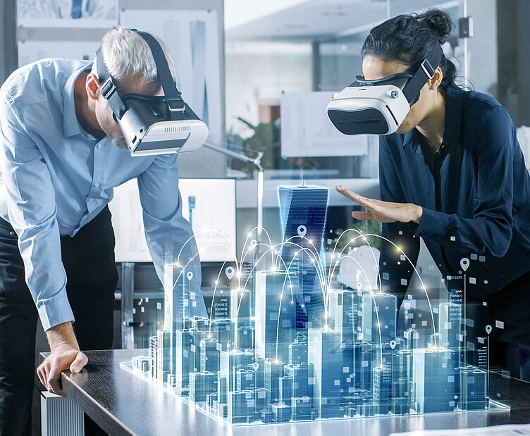 Zwei Personen mit VR-Headsets betrachten ein holografisches 3D-Stadtmodell auf einem Tisch, das eine vernetzte Smart City darstellt.