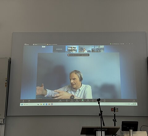 Josef Bernhart hält seinen Vortrag zur Entbürokratisierung per Videoschalte auf einer Leinwand.