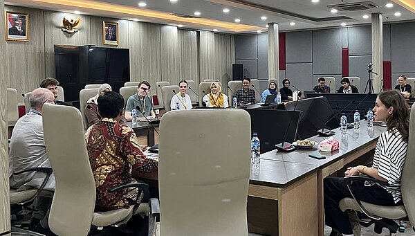 Studierende und Forschende sitzen an einem großen U-förmigen Tisch zur Diskussion.