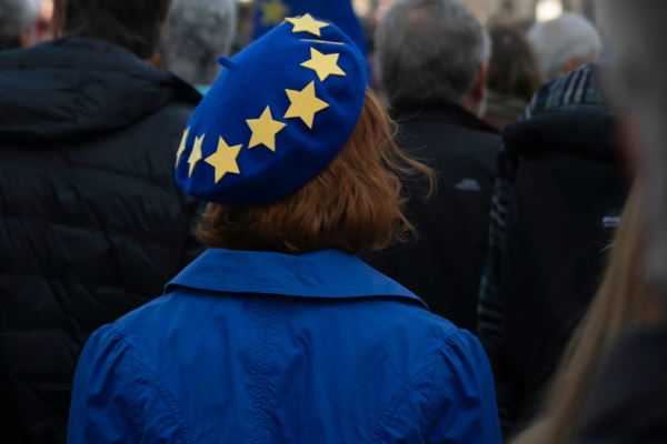 Frau mit blauem EU-Barett in einer Menschenmenge bei einer pro-europäischen Demonstration auf dem Trafalgar Square in London, im Hintergrund sind Gebäude und eine EU-Flagge sichtbar.