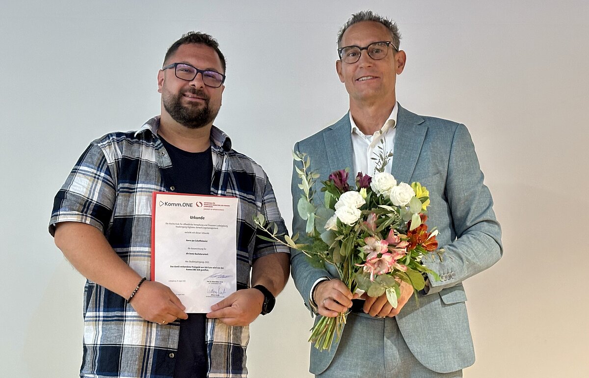 Jan Scheffelmeier (l.) hält eine Urkunde und William Schmitt (r.) einen Blumenstrauß. Sie posieren lächelnd nebeneinander.