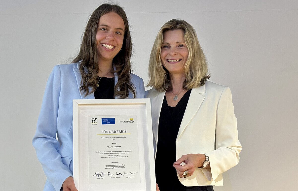 Alina Kustermann (l.) und Heidi Schmid (r.) posieren mit einem gerahmten Förderpreis-Zertifikat. Beide lächeln.