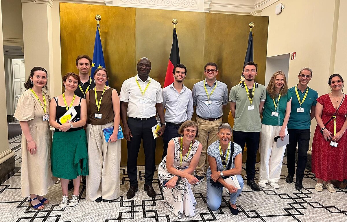 Gruppenfoto von 15 Teilnehmenden vor den Flaggen der Europäischen Union, Deutschlands und der Landesflagge Baden-Württembergs.