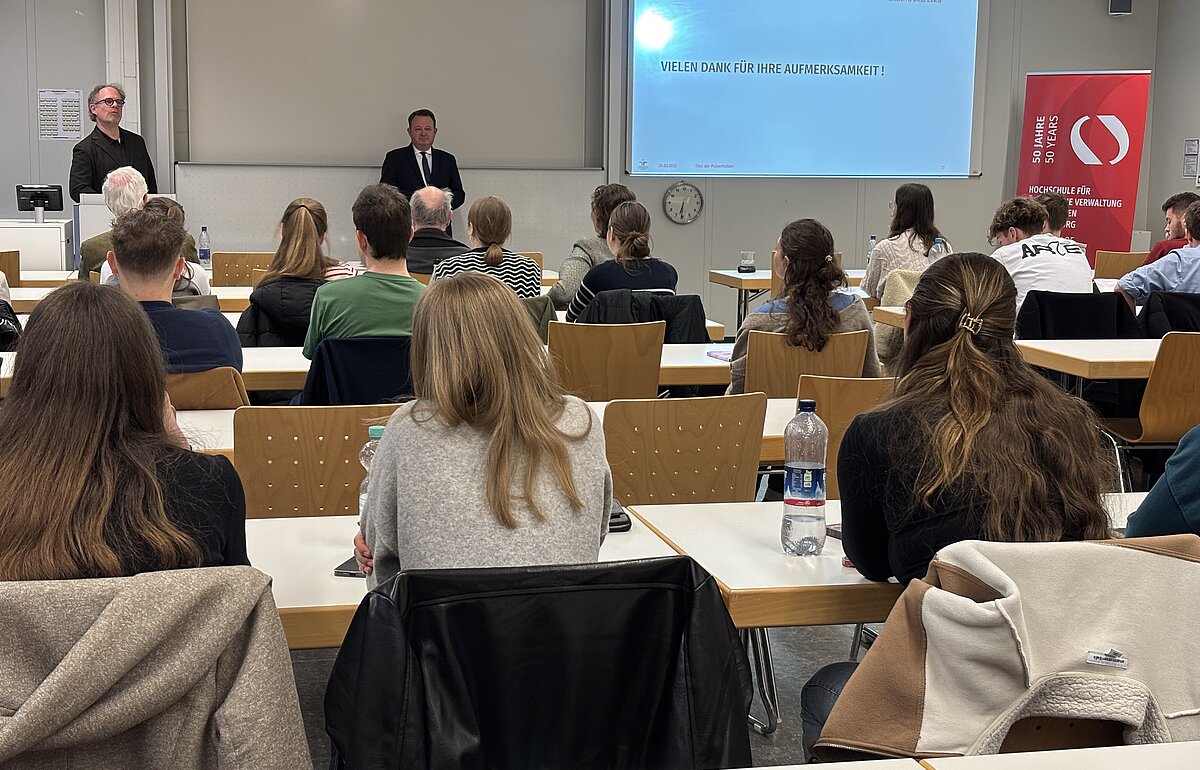 Zwei Männer, links Prof. Dr. Volker Haug, rechts Prof. Dr. Arne Pautsch, stehen in einem gefüllten Seminarraum. Hinter ihnen eine Leinwand auf der "vielen Dank für Ihre Aufmerksamkeit" steht.