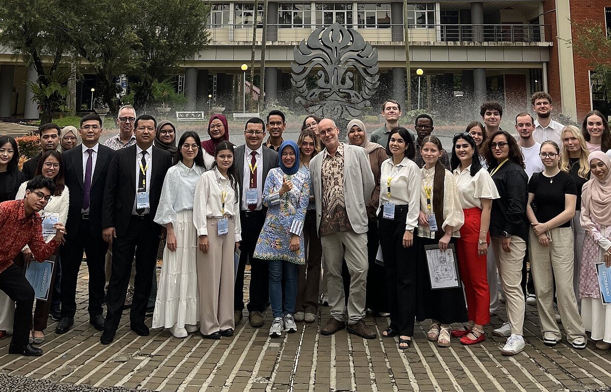 Große Personengruppe der HVF und Universitas Indonesia vor einem modernen Campusgebäude mit Brunnen und Palmen in Jakarta. 