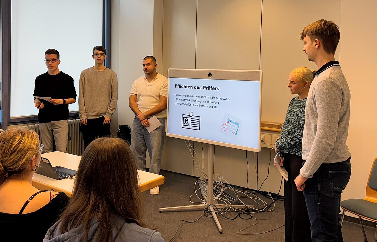 Vier Studierende präsentieren vor einem kleinen Publikum im Finanzamt Stuttgart-Körperschaften ihren Leitfaden zu den Pflichten des Prüfers für neu eingesetzte Umsatzsteuerprüfer:innen