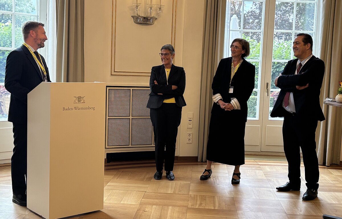 Holger Stegmaier spricht bei der Ordensverleihung an Prof. Dr. Angelika Dölker, neben ihr stehen der französische Generalkonsul Gaël de Maisonneuve und eine weitere Person in einem festlichen Raum